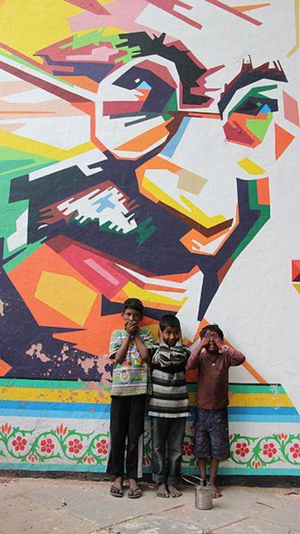​Three kids in front of a street art portrait of Gandhi