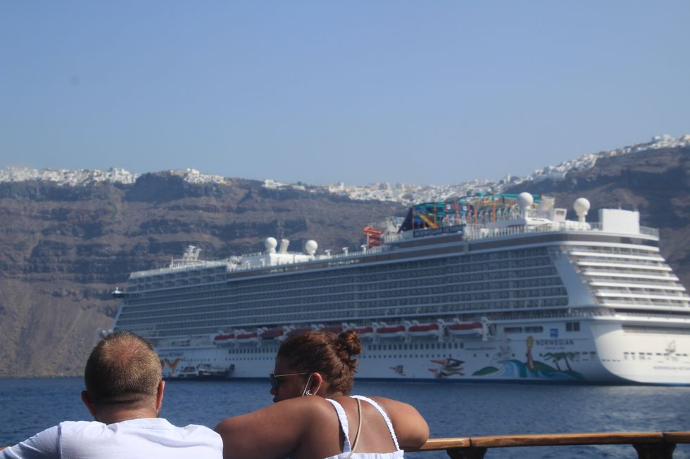 ​Tourists look at a huge cruise ship in front of the popular Greek vacation island of Santorini.