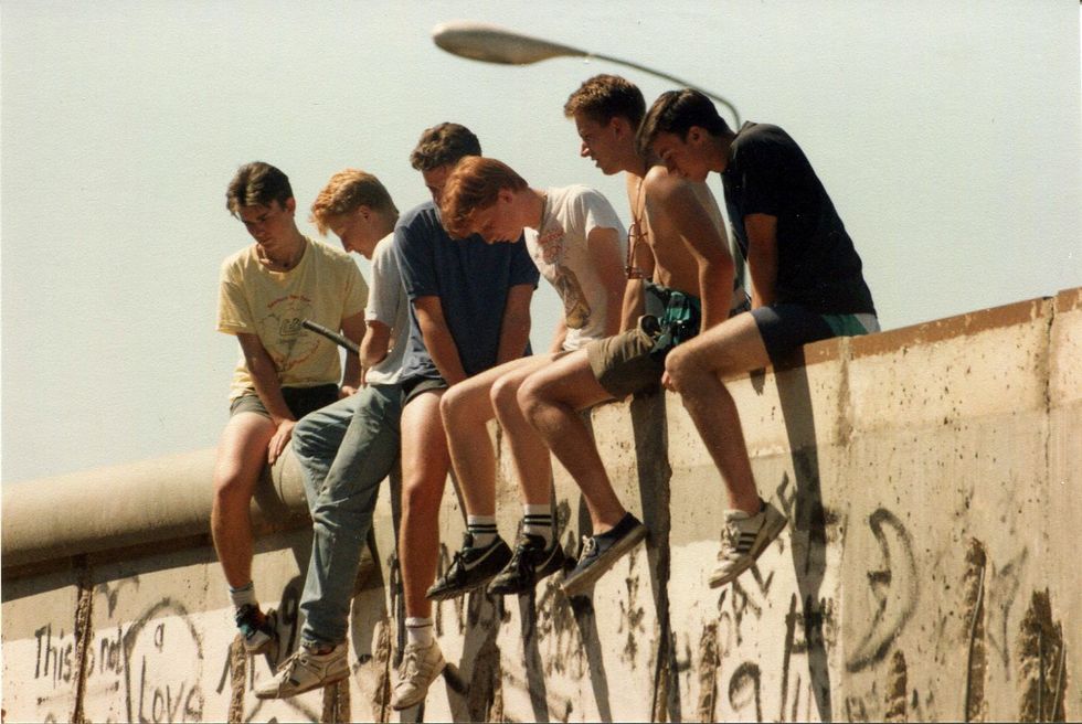 ​Young men sit on top of the Berlin Wall in October 1990, days before the German Reunification is officially proclaimed.