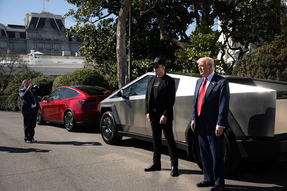 Elon Musk and Donald Trump standing in front of a Tesla Cybertruck and a red Tesla Model Y outside a government building.