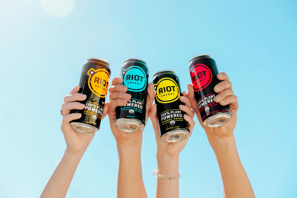 Energy drink cans held by people, with the sky in the background.