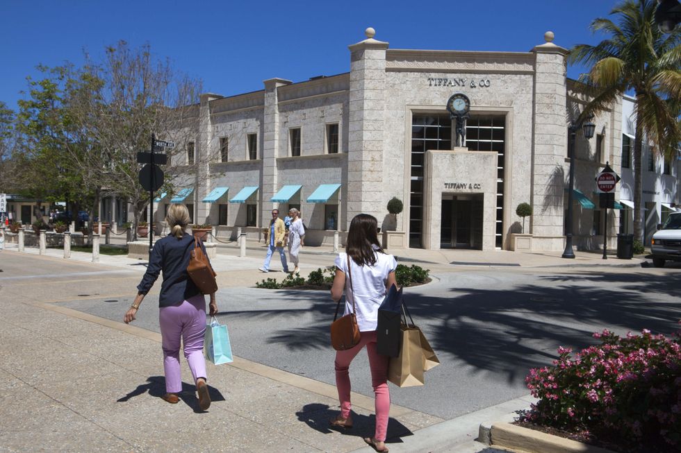 Female pedestrians carrying shopping bags walk past a Tiffany & Co store on Worth Avenue, Palm Beach, USA.