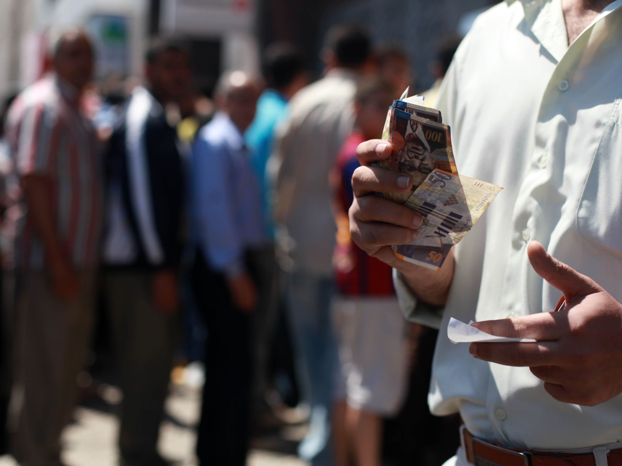 File photo of people queuing to withdraw money from an ATM in Gaza City, with a man counting his money in the foreground.