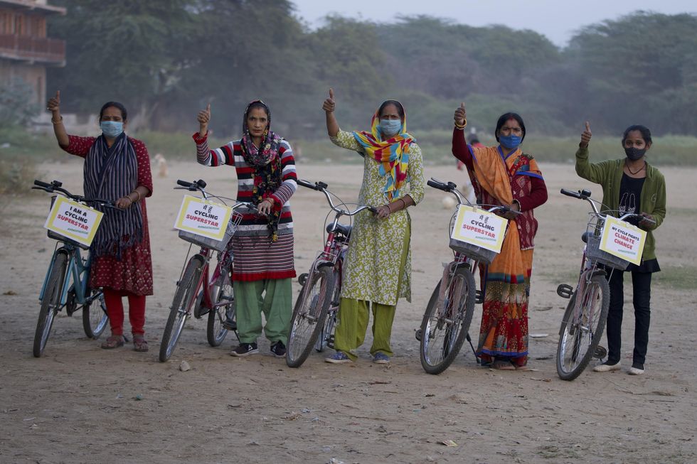 Five Indian women hold their fist in the air while standing next to their bikes.