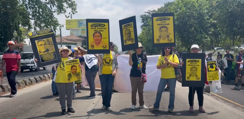 Five women stand in a street holding yellow signs and wearing yellow t shirts, protesting