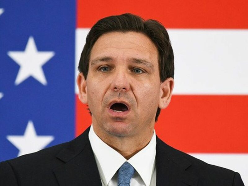 Florida Governor Ron DeSantis in front of a U.S. flag, open-mouthed.