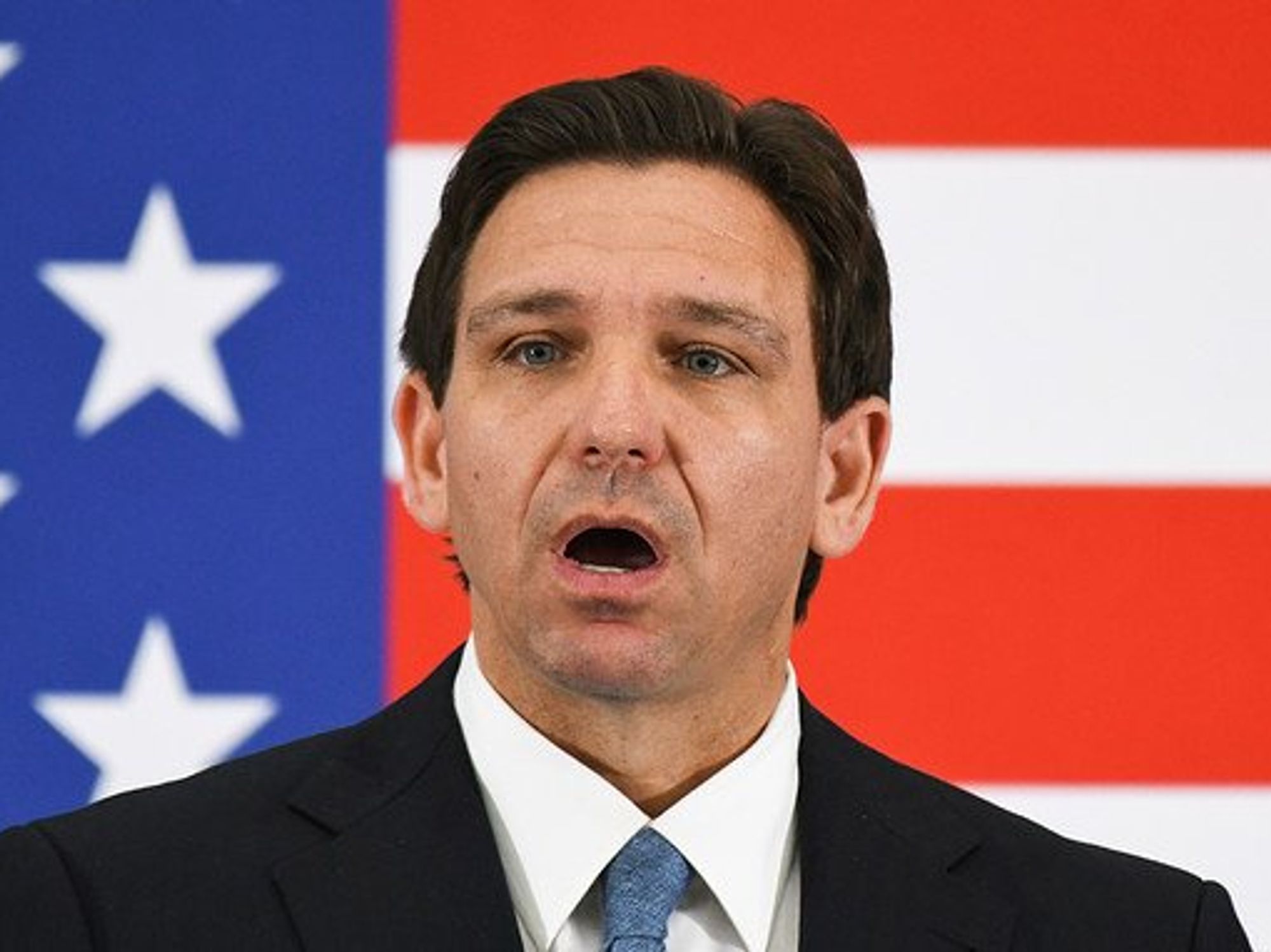 Florida Governor Ron DeSantis in front of a U.S. flag, open-mouthed.