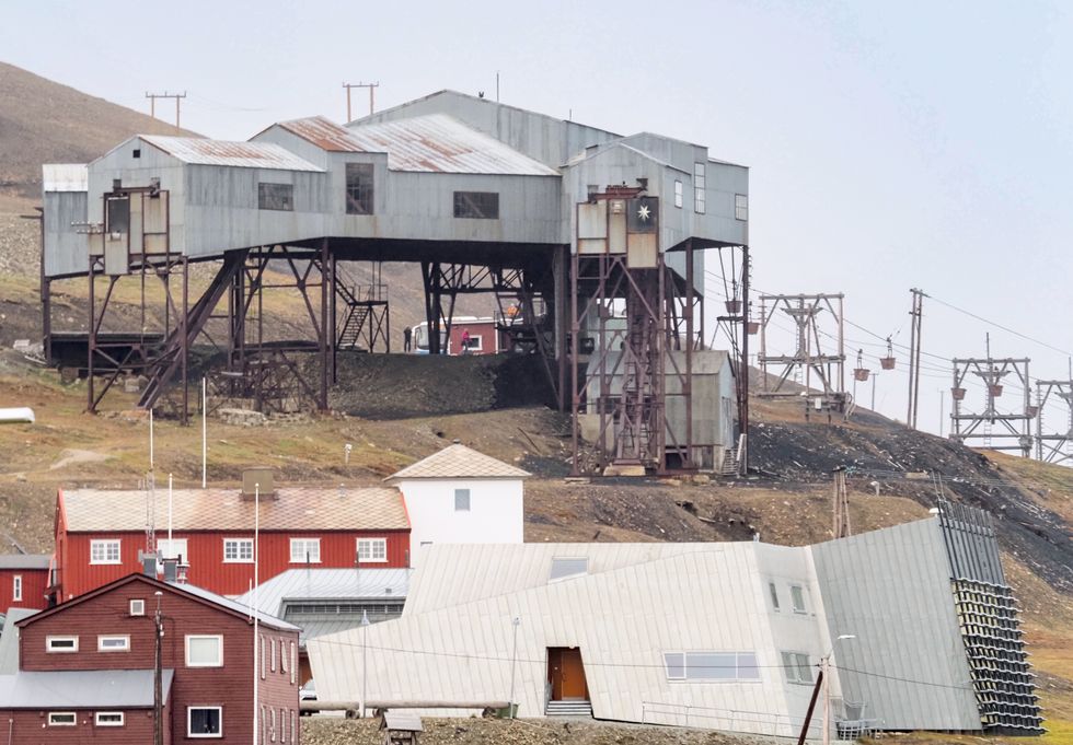 Foreground of red houses on the side of a mountain. At the top of the photo is the old power station and power lines can be seen in the distance.