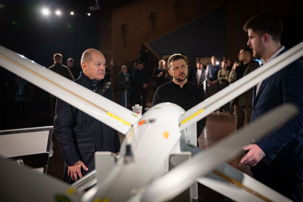 German Chancellor Olaf Scholz and Ukrainian President Volodymir Zelensky stand behind a military drone.