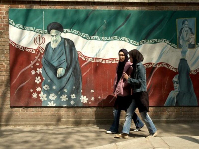 Girls in western jeans walking past a picture of Ayatollah Khomeini in Tehran
