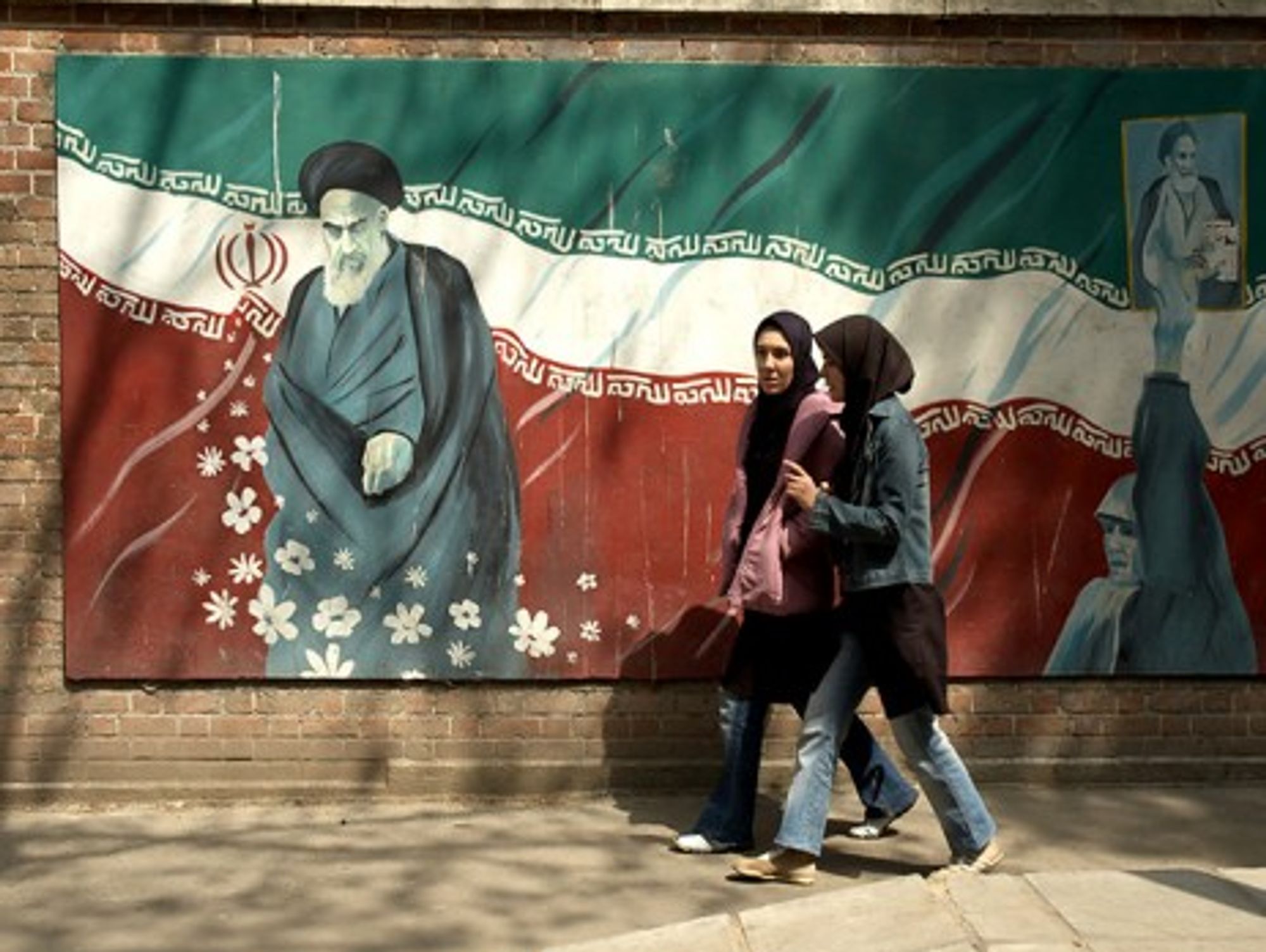 Girls in western jeans walking past a picture of Ayatollah Khomeini in Tehran