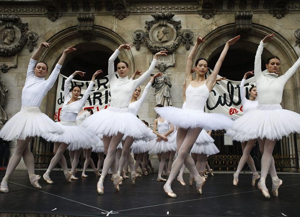 Group photo of Paris Opera dancers in white tutus dancing in front of the Palais Garnier, with placards in protest of the French government's plan to overhaul retirement age
