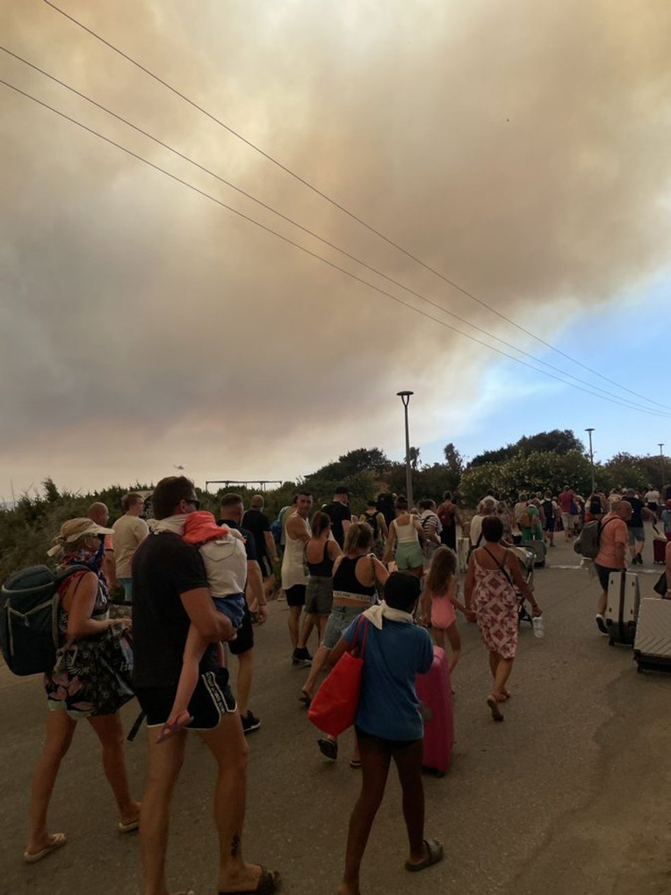Holidaymakers in Rhodes flee their resort with luggage in hand as wildfires cross the island