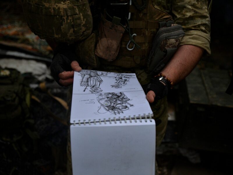 Image depicting a Ukrainian soldier displaying his artistic drawings depicting life in the Ukrainian military during the war