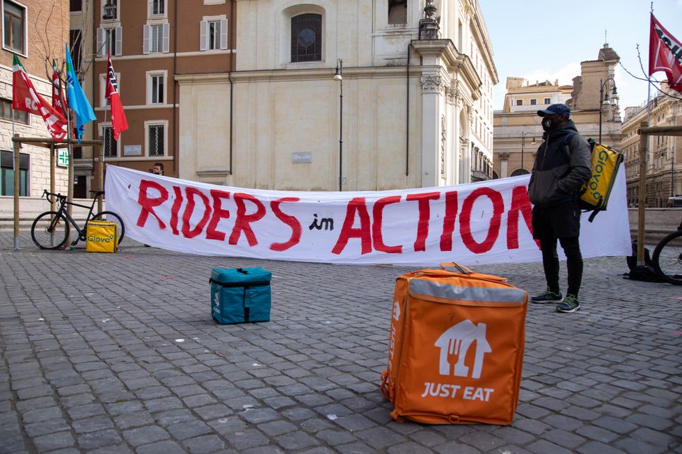 Image of a banner saying "Riders in Action", next to some food delivery cool bags, in Rome.