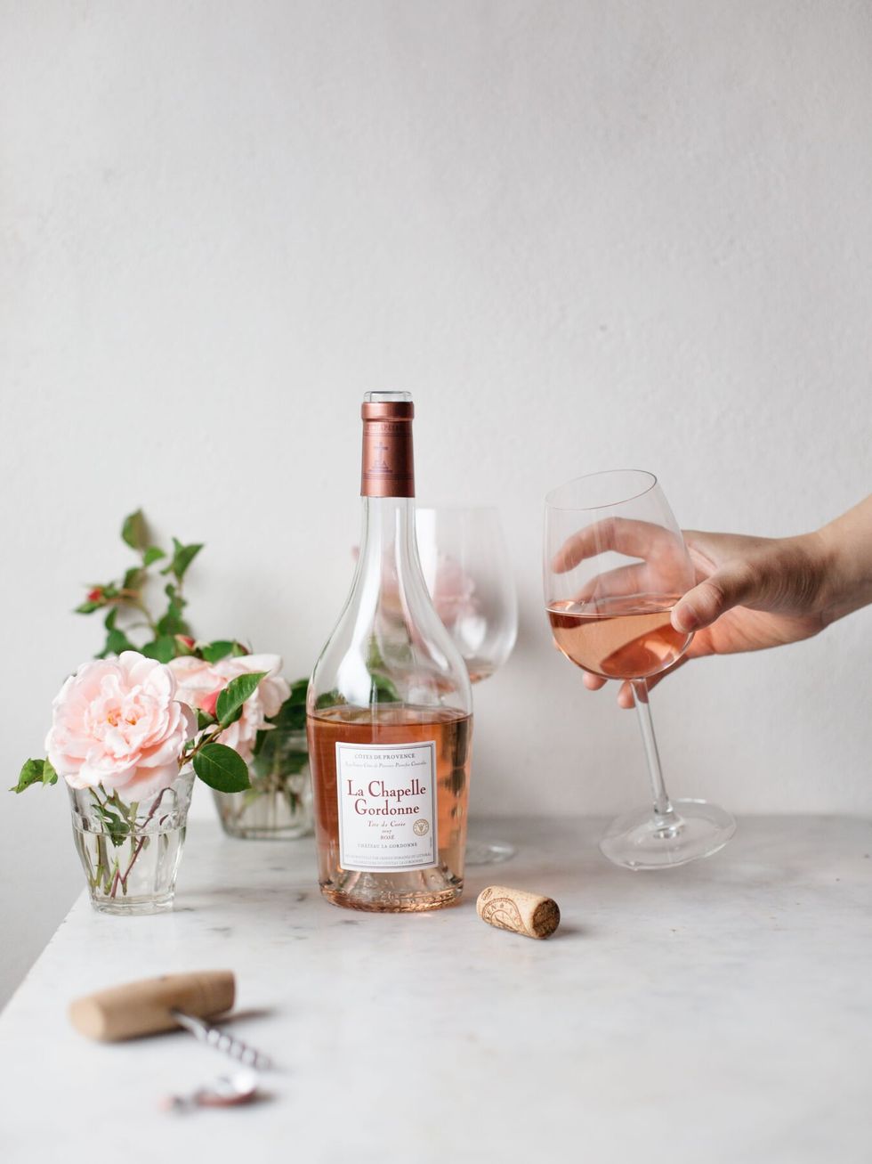 Image of a bottle of rosé with someone holding a glass full of wine next to it.