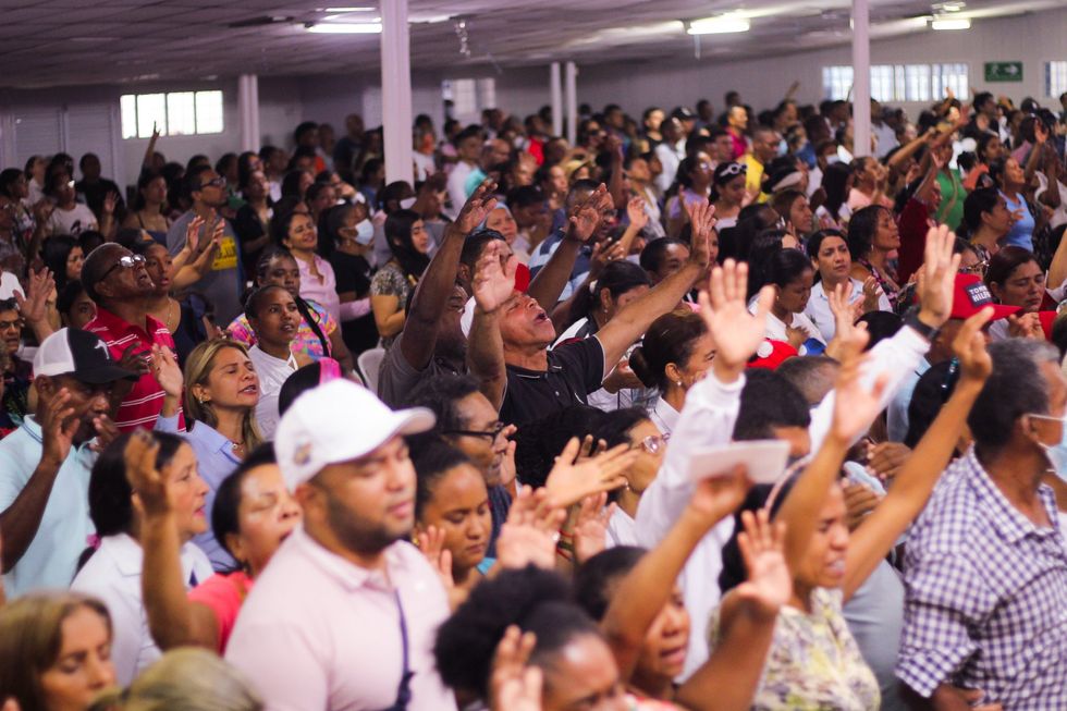 Image of a crowd in a church raising their arms in the air in approval of the speech given by Esteban Acosta.