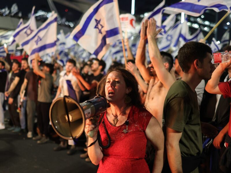 Image of a crowd of protestors holding Israeli flags and a woman speaking into a megaphone