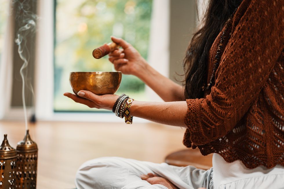 Image of a ​woman using a Tibetan singing bowl and burning incense.
