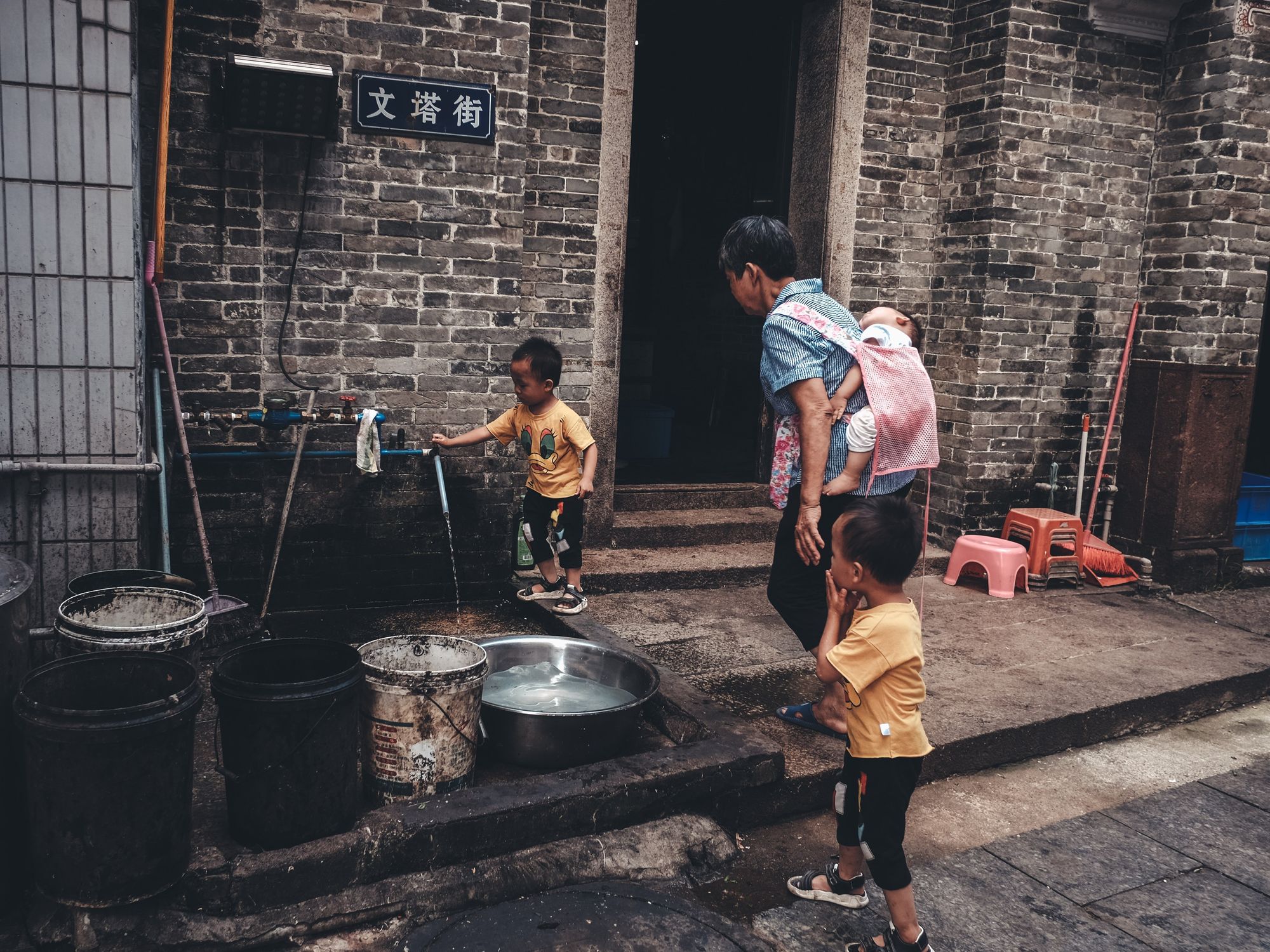 Image of a father watching his child play with water, carrying a child on his back, and holding his other kid's hand.