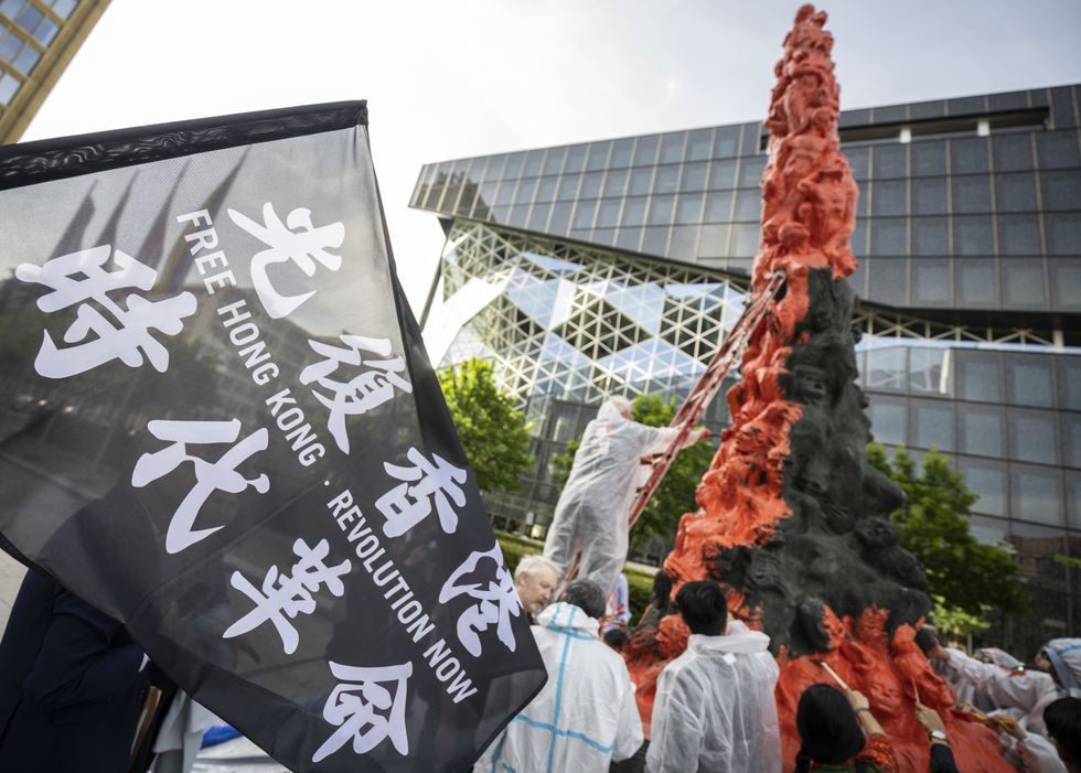 Image of a flag with the inscription ''Free Hong Kong - Revolution Now'' being held high during the painting action in front of the ''Pillar of Shame'' memorial in Berlin, Germany.