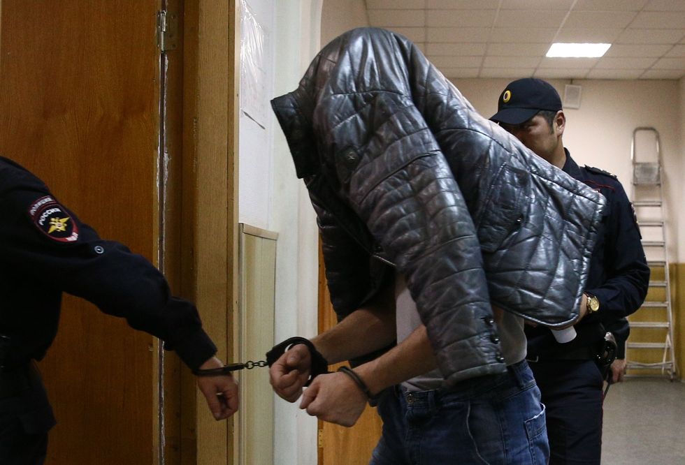 Image of a handcuffed man whose face is covered by his jacked is being dragged by the police into a courtroom.