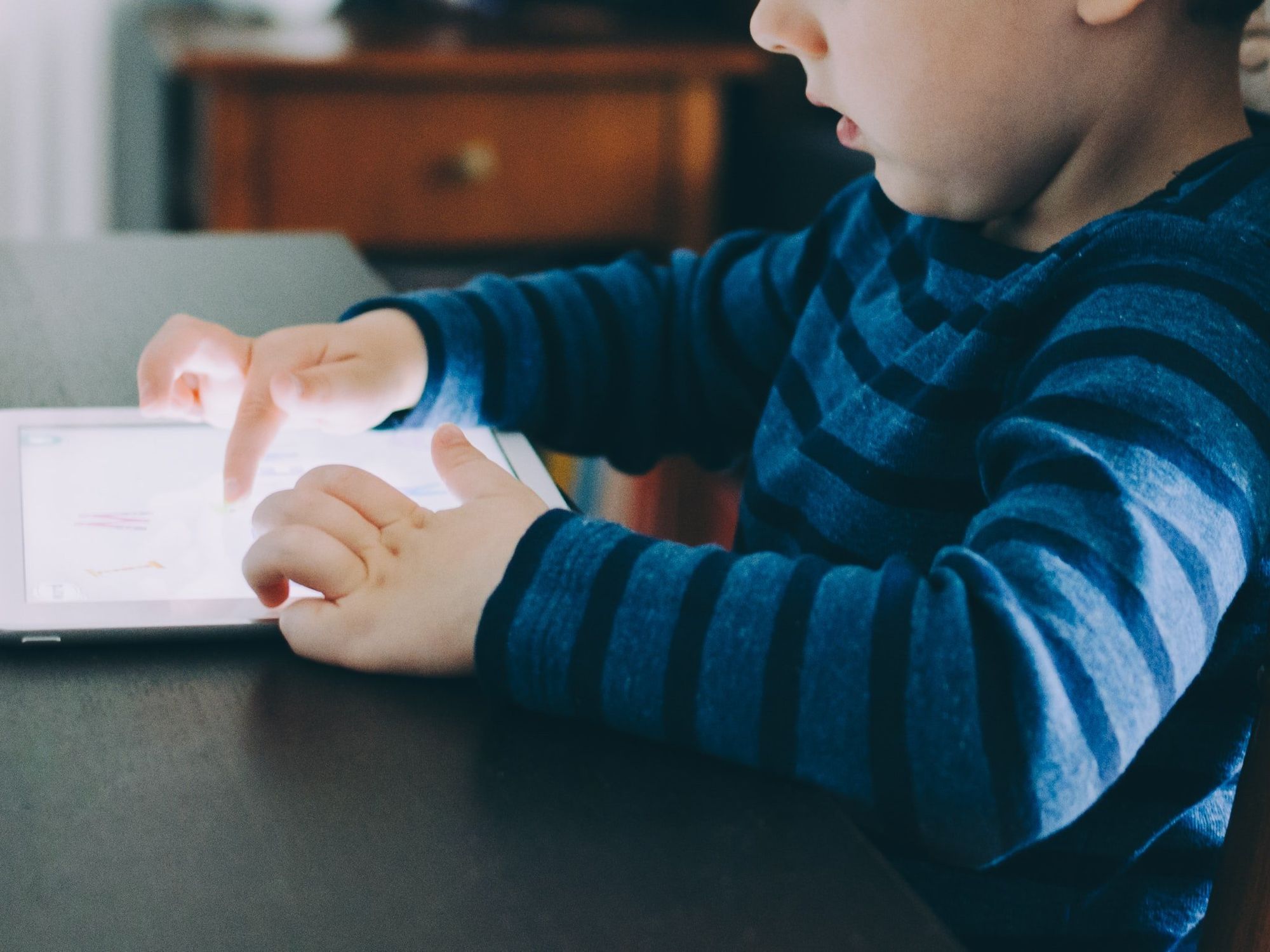 Image of a kid wearing a blue striped sweater, using an ipad.