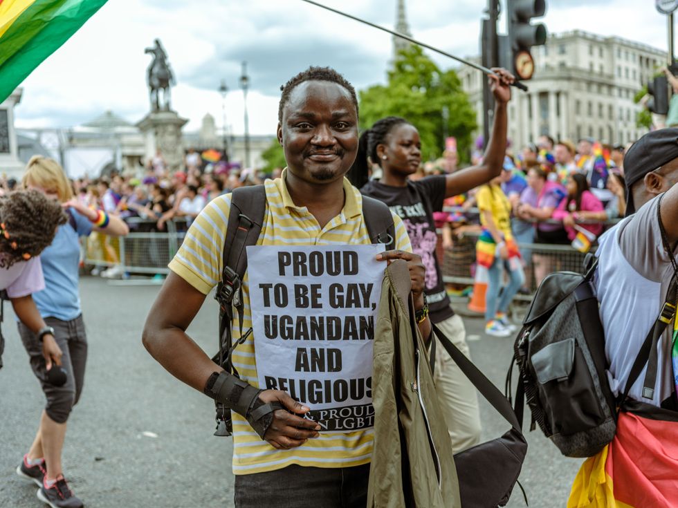image of a man holding a sign saying "proud to be gay, Ugandan and religious" at a pride march
