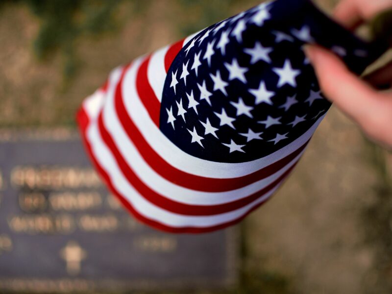 Image of a person holding the national flag of the United States in front of a grave.