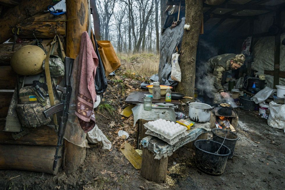 Image of a soldier's camp in the middle of the forest, where a Ukrainian soldier is cooking his dinner on an improvised kitchen.