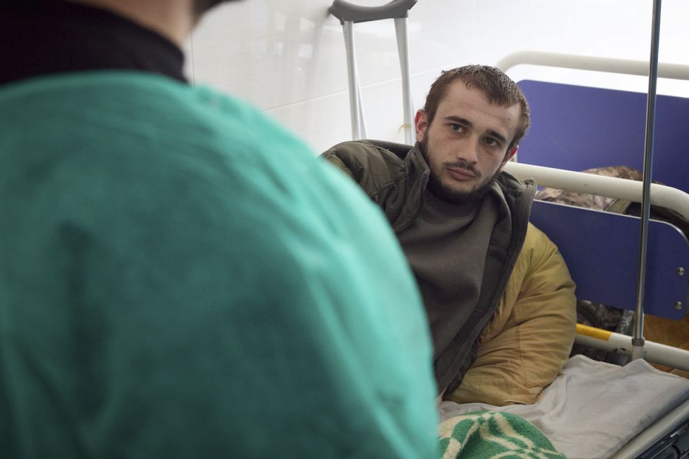 Image of a ukrainian soldier laying in a hospital bed facing ukrainian president volodymyr zelensky