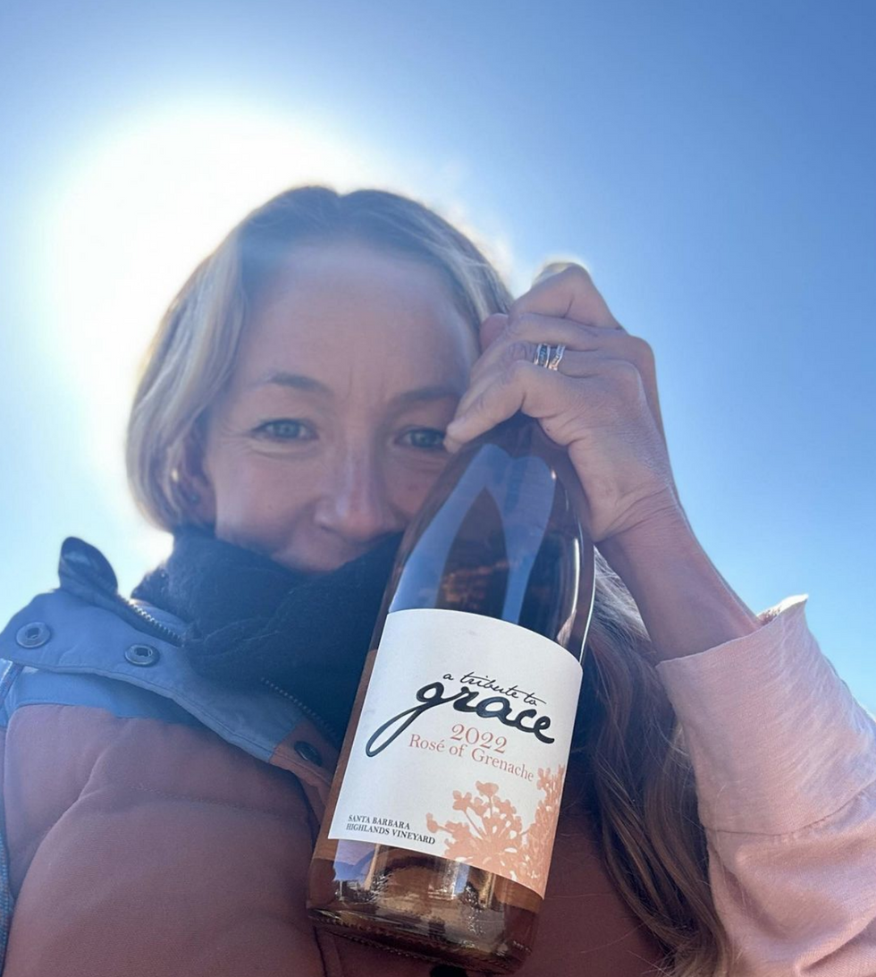 Image of a woman (Angela Osborne) holding a bottle of the wine she produces.