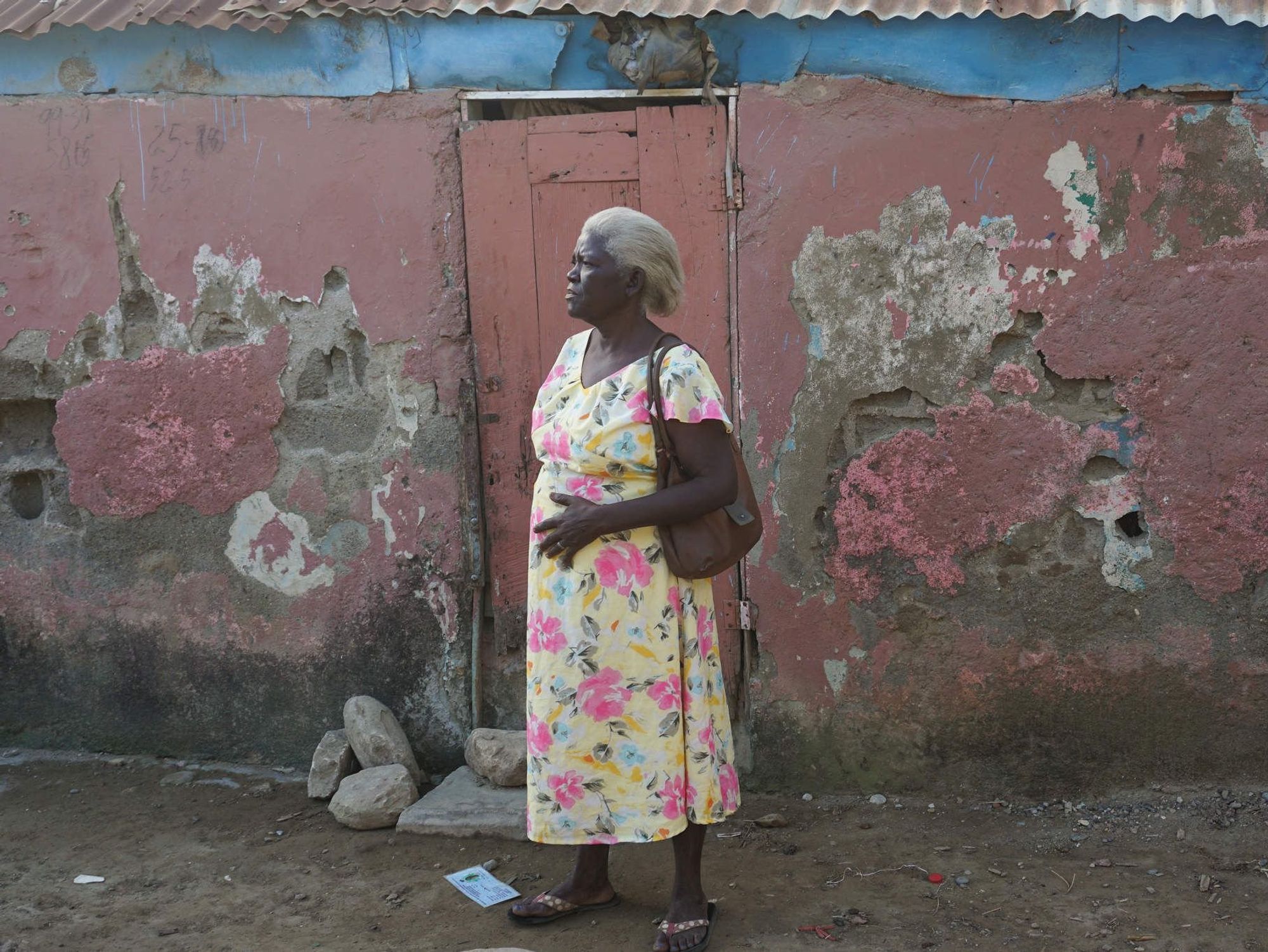 Image of a woman standing outside her home damaged by flooding.