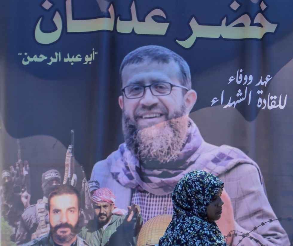 Image of a woman walking in front a big picture representing Khader Adnan.