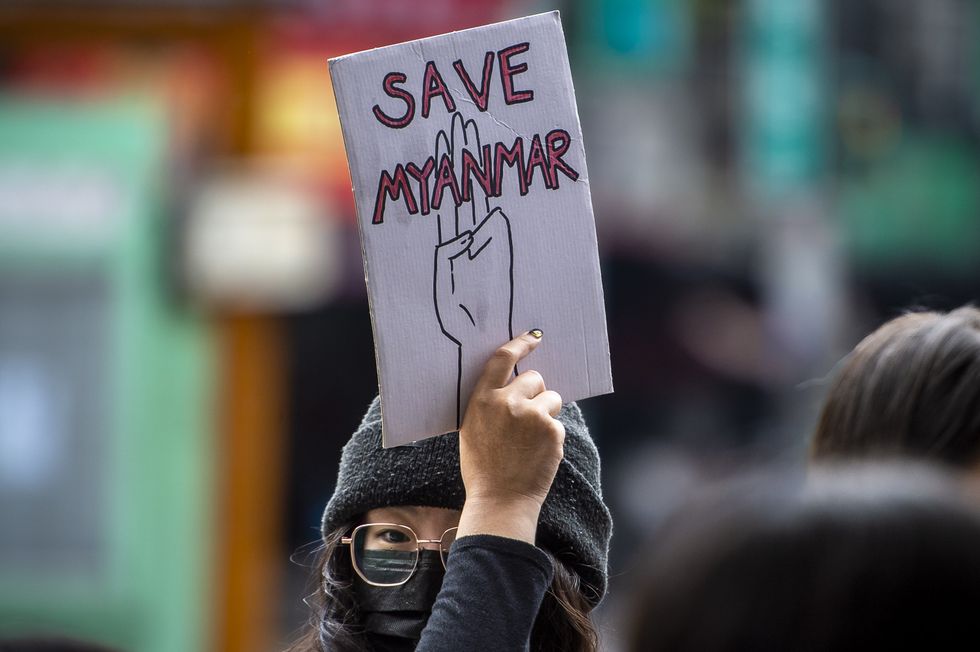 Image of a woman wearing a hat and a face mask, holding a sign that says "Save Myanmar" during a protest in Taiwan.