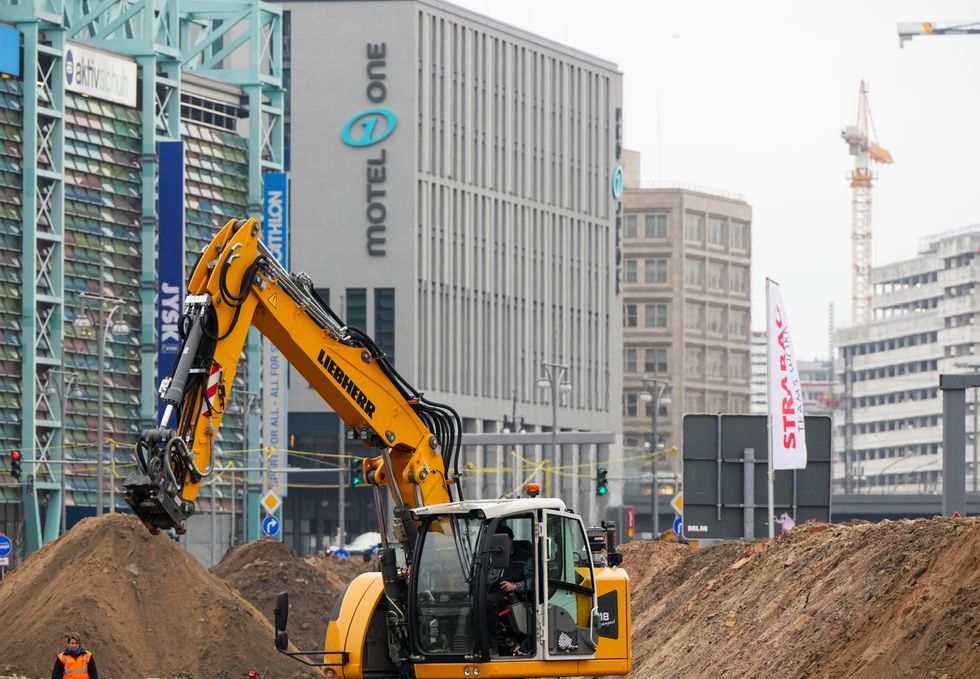 Image of a yellow construction machine operating between mountains of sand at a construction site in the city.