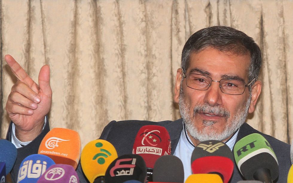 Image of Ali Shamkhani, Secretary of Iran's Supreme National Security Council, during a press conference, speaking into microphones held out by several journalists.