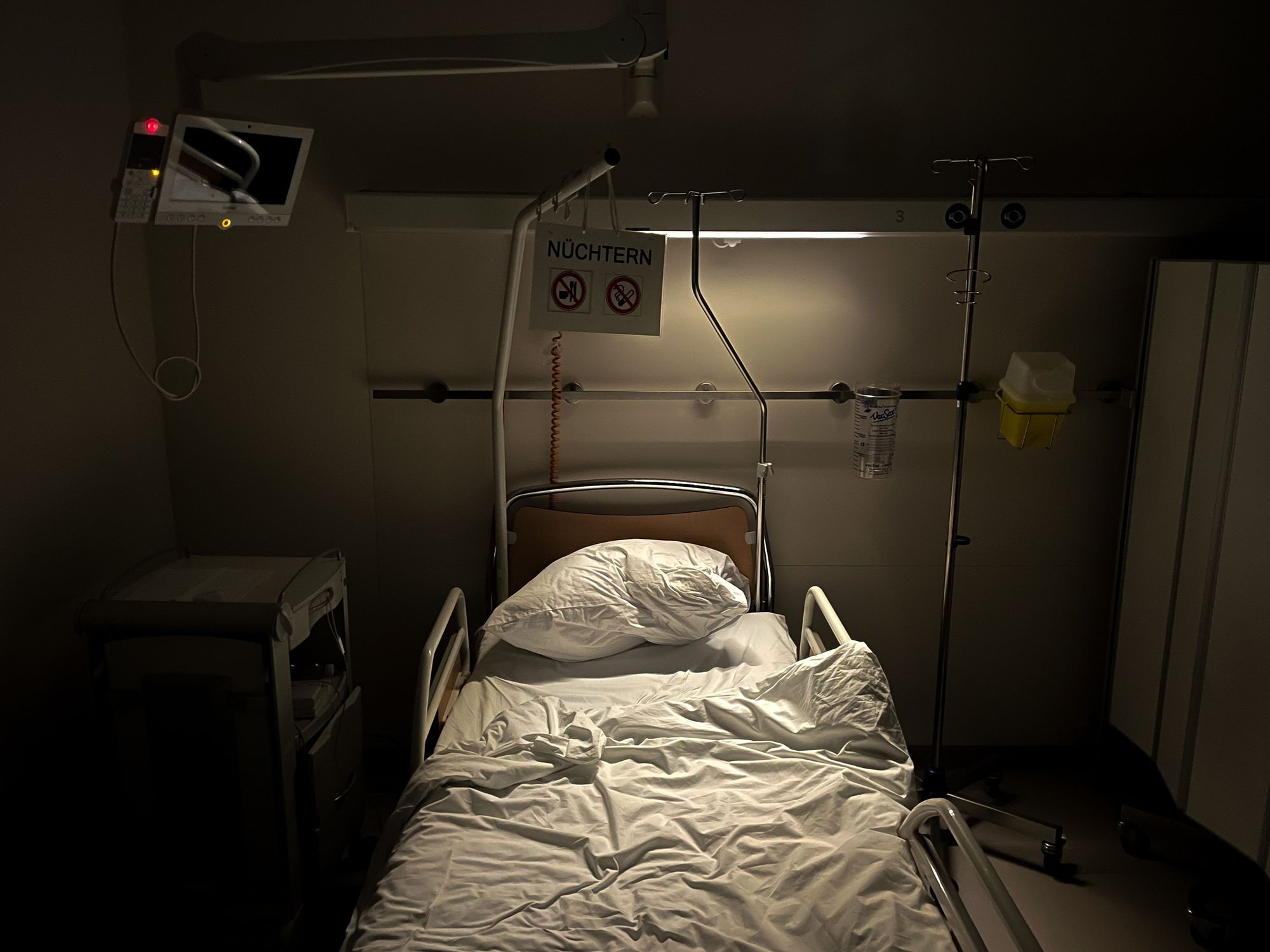 Image of an unmade hospital bed in a dimly lit hospital room.