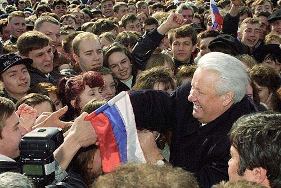 Image of Boris Yeltsin interacting with a crowd and shaking the hand of a citizen holding a Russian flag.