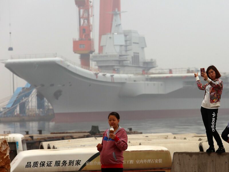 Image of Chinese girls taking selfies with China's second aircraft carrier, currently called the 001A, parked in a shipyard in the port city of Dalian in Liaoning Province, China.