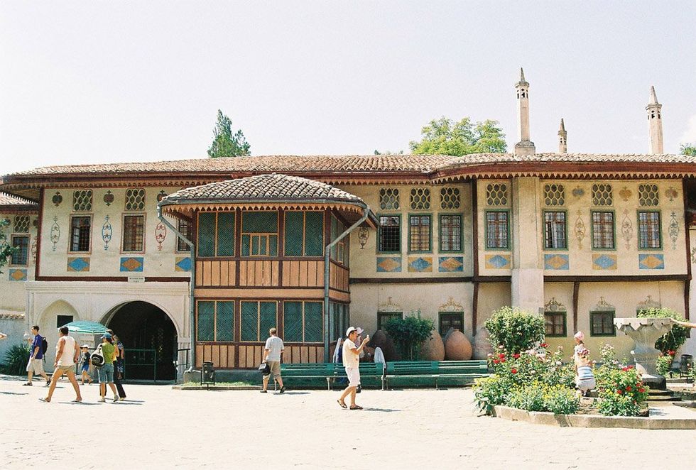 Image of ​Living quarters of Hansaray in Bakhchisaray, Crimea. People are dressed in summer clothing and walking around.