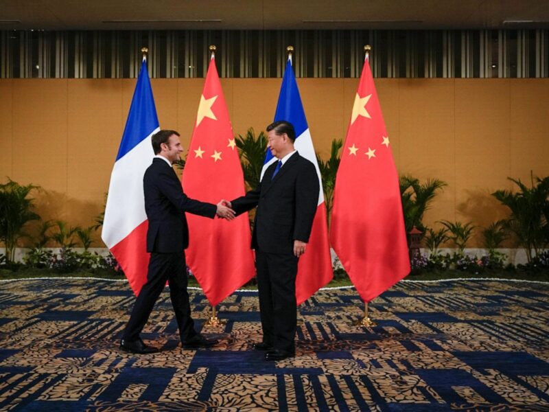 Image of French President Emmanuel Macon and Chinese President Xi Jinping shaking hands with a french and chinese flag in the background