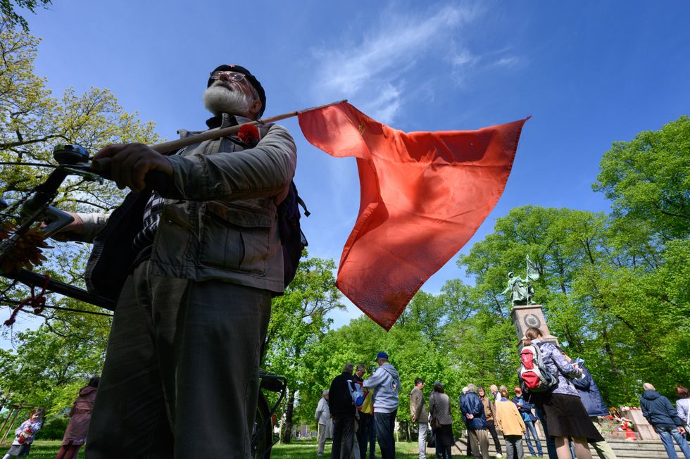 Image of Hans-Jürgen Westphal, political activist, standing with a flag of the former Soviet Union, at a commemoration ceremony for Liberation Day at the Red Army Memorial.