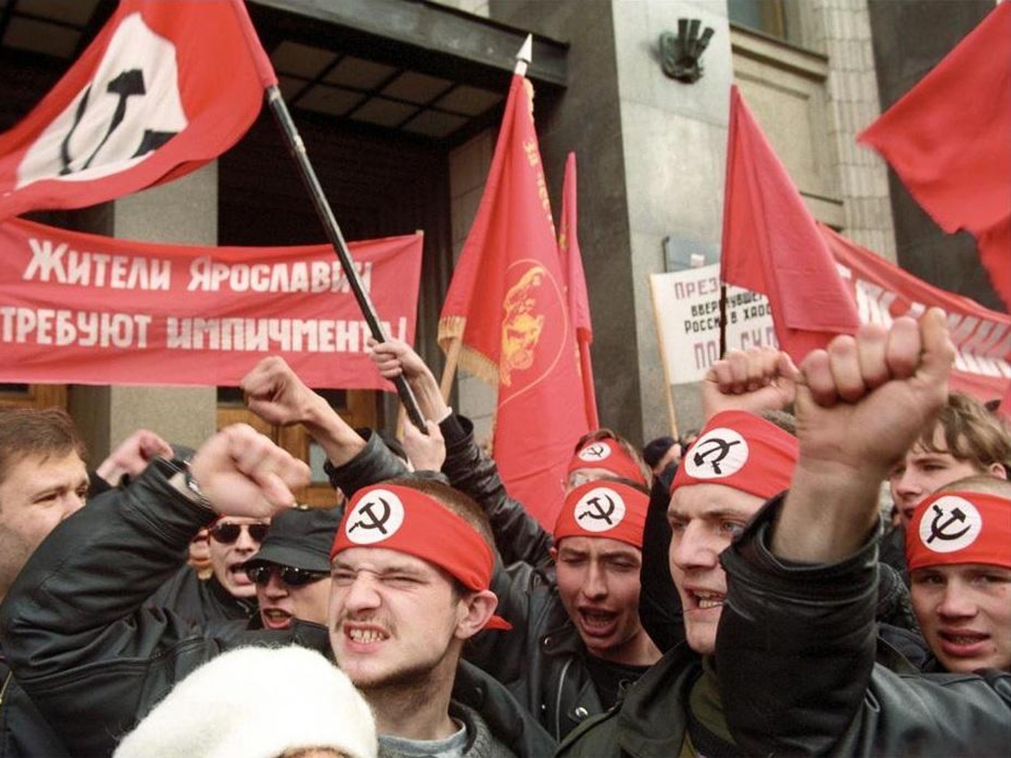 Image of people marching, wearing headbands with USSR flags and holding USSR flags in protest.