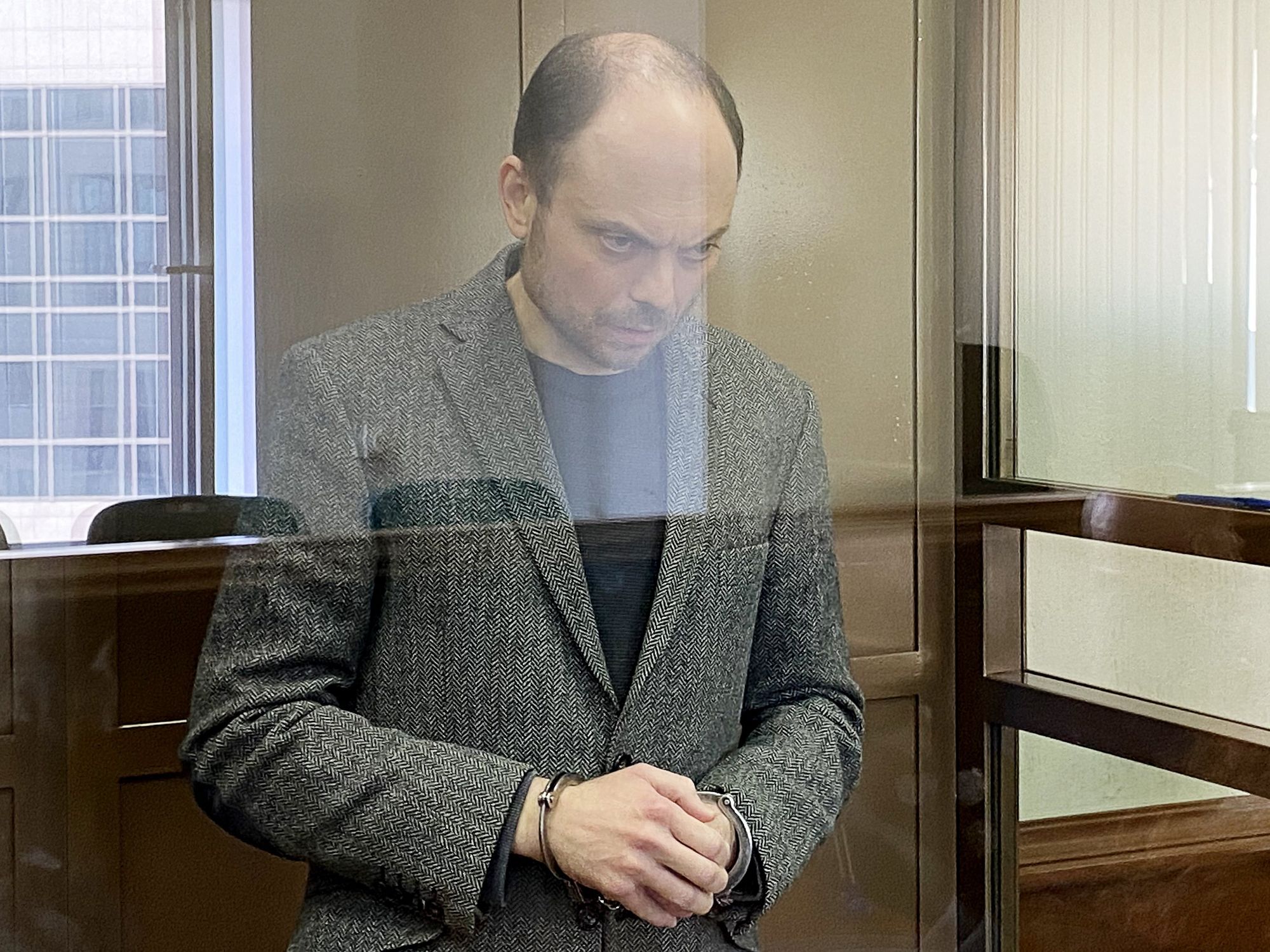 Image of Russian political activist Vladimir Kara-Murza in a formal attire, handcuffed and staring intently ahead.