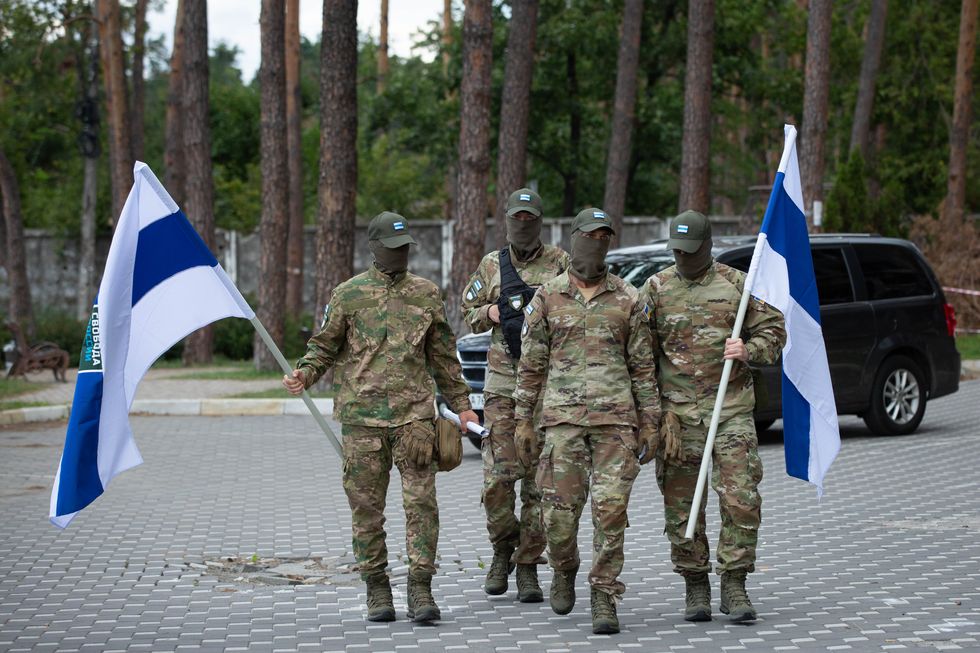 Image of Russian soldiers walking on the strees holding blue and white flags of the Russian Legion "Freedom of Russia"