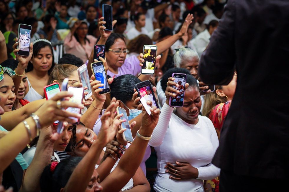 Image of several people, mostly women, crying and holding out their phones to show images of their relatives to Esteban Acosta.