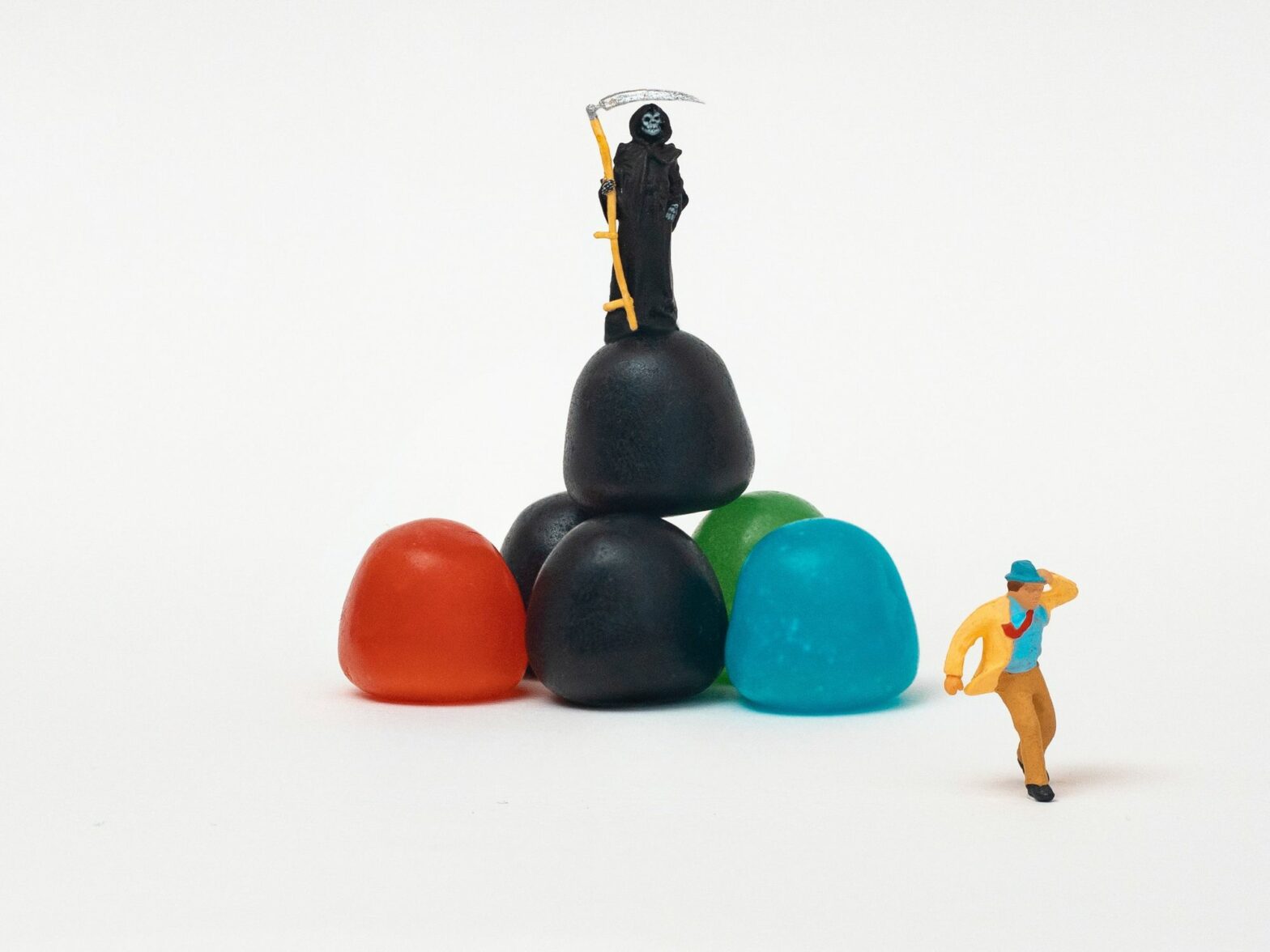 Image of six colorful candies, on which a mini statue of death is standing, looking at a man running away.