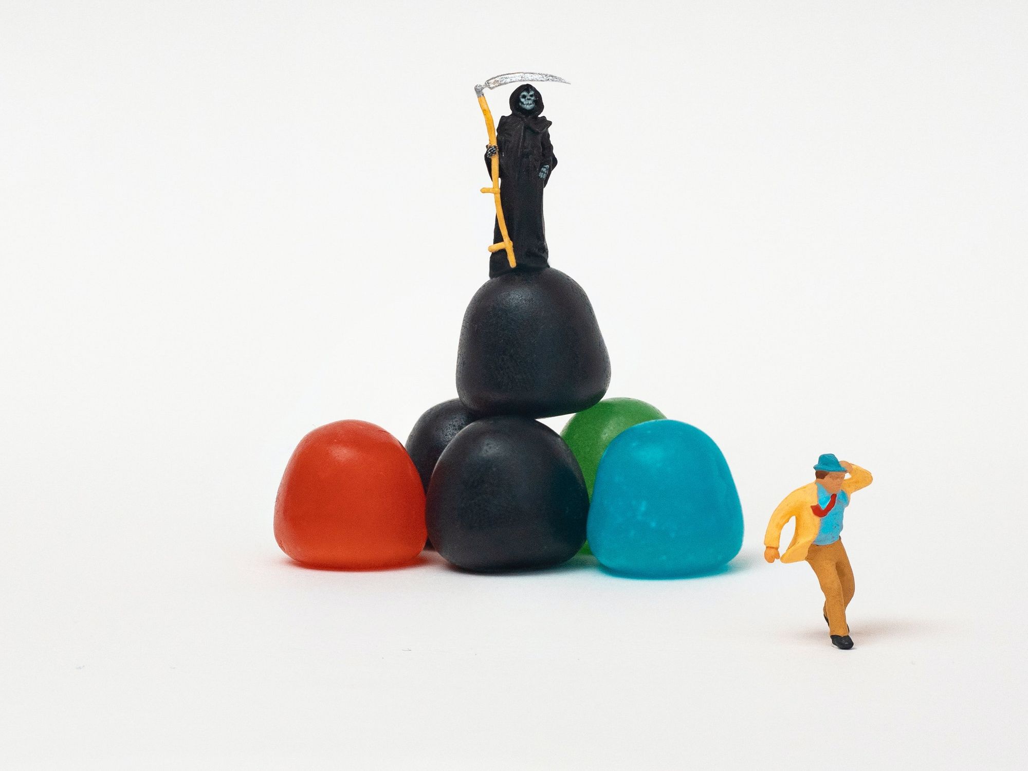 Image of six colorful candies, on which a mini statue of death is standing, looking at a man running away.