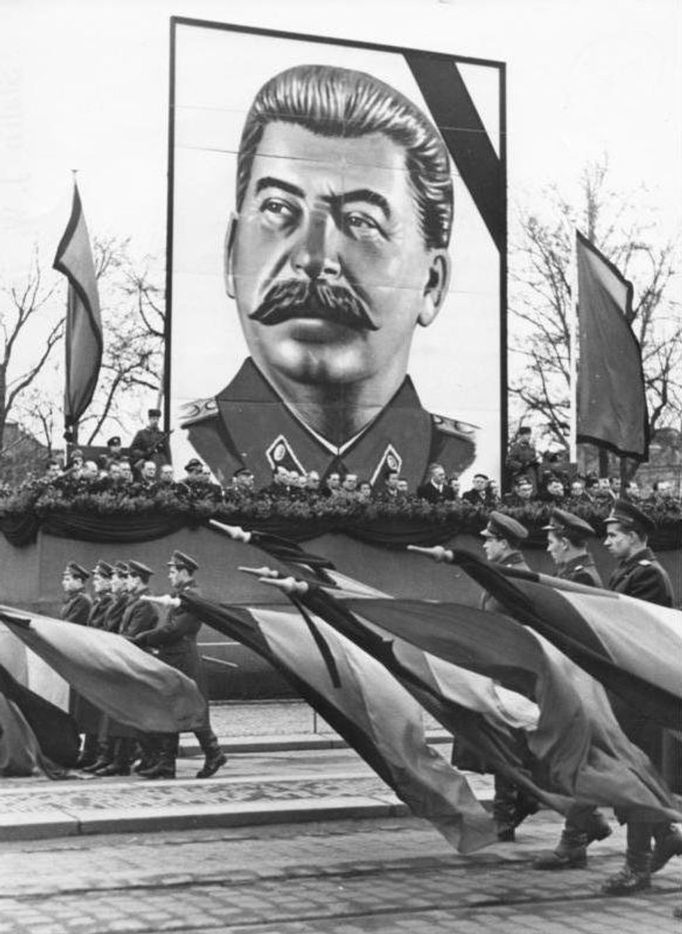 Image of soldiers parading in front of a huge portrait of Stalin